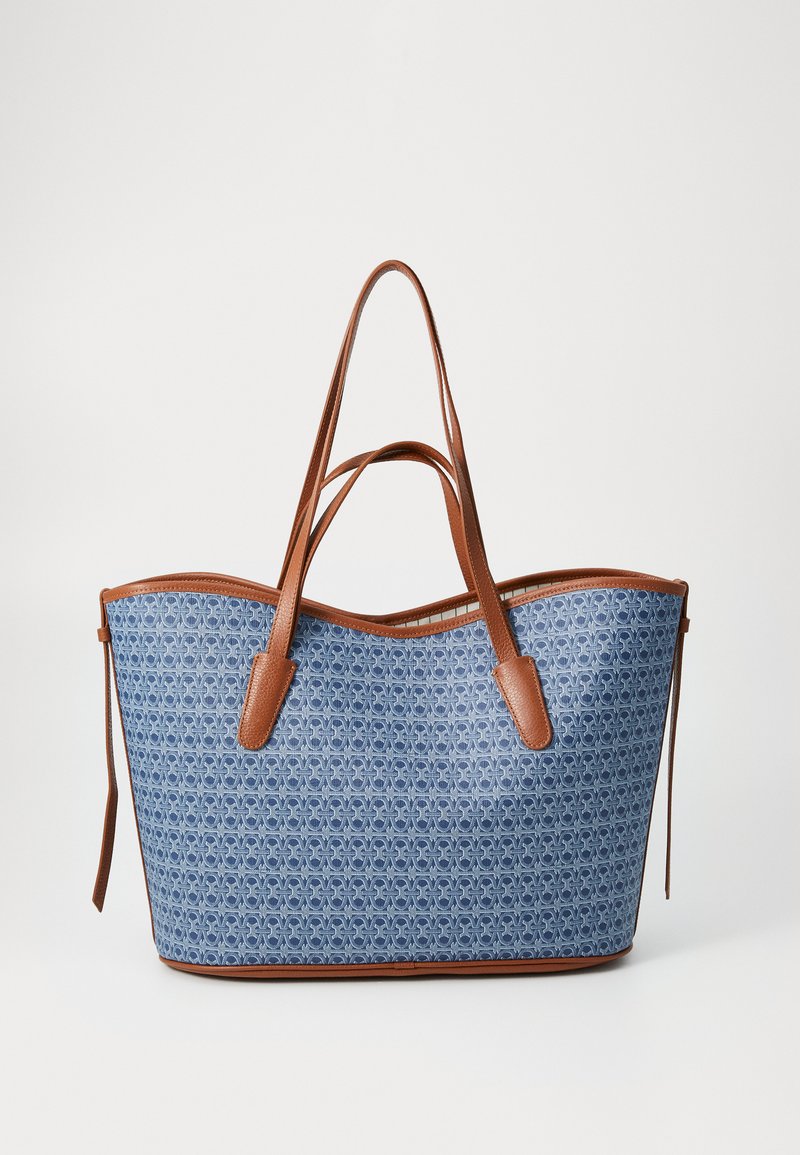 Blue patterned tote bag with brown leather handles and accents. Curved top edge and open design, offering a spacious interior.