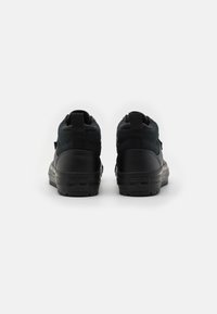 Adidași negri cu o combinație de piele netedă și material texturat, formă rotunjită, suport înalt pentru gleznă și etichete de prindere la călcâi.