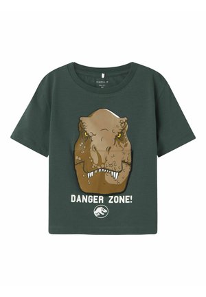 Camiseta de algodón verde con un gráfico de dinosaurio, que presenta la cabeza de un T-rex marrón y texto blanco que dice "¡ZONA PELIGROSA!" en la parte inferior.