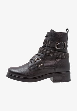 Schwarze Leder-Ankle-Boots mit strukturiertem Finish, zwei verstellbaren Riemen mit Nieten, Metall-Schnallen und einem klobigen Absatz.