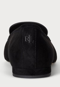 Fekete velúr slip-on cipők kerek orral, törtfehér talppal és dombornyomott „RL” logóval a hátsó sarkán. Simás, textúrázott felület.