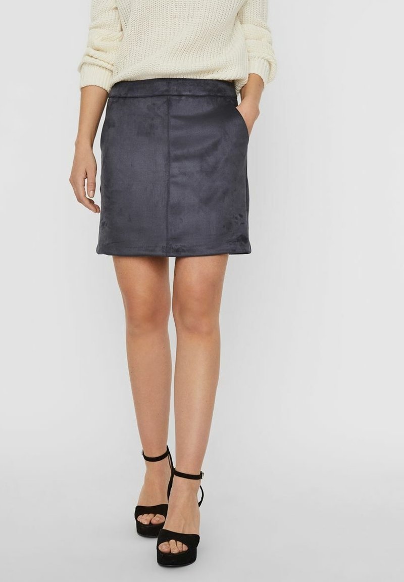 Mini falda de ante sintético gris oscuro con una textura suave, corte recto y bolsillos laterales, combinada con sandalias de tacón alto negras.