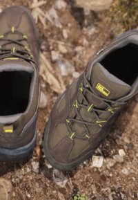 Scarpe da trekking marroni con una parte superiore testurizzata, dettagli gialli e suola in gomma durevole. Presentano un design con lacci e un collare imbottito per il supporto.