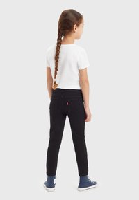 Pantalons en denim noir avec une coupe slim, dotés de poches arrière et d'une étiquette rouge. Associés à un t-shirt blanc et des baskets montantes bleues.