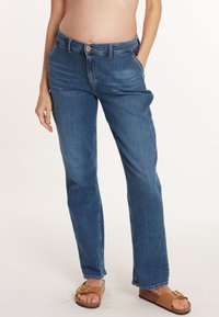 Jeans en denim bleu clair avec une coupe droite, cinq poches et une fermeture à bouton à l'avant. Portés avec des sandales marron pour le contraste.