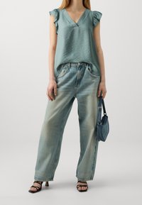 Světlý tyrkysový top s výstřihem do V a nařasenými rukávy, doplněný světlomodrými širokými kalhotami. Dopl�ňky zahrnují malou džínovou tašku a černé vysoké sandály.