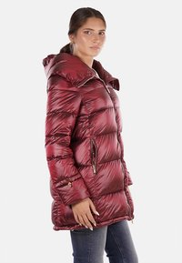 Giacca imbottita bordeaux con cappuccio, chiusura a zip e tasche laterali. Texture liscia e lucida con motivo trapuntato e dettagli in hardware dorato.