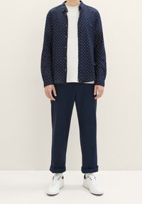 Mörkblå mönstrad skjorta med knappar över en vit t-shirt, kombinerad med mörkblå byxor och vita sneakers. Slät tyg, avslappnad passform.