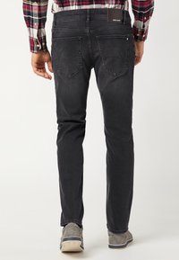 Jeans in denim nero con vestibilità slim, dotati di cinque tasche e di un'etichetta marrone in vita. Indossati con scarpe grigie, mostrano una texture liscia.
