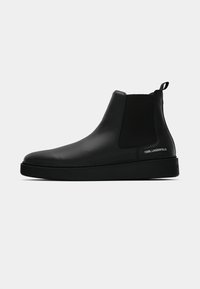 Botas de tornozelo em couro preto com painéis laterais elásticos, bico arredondado e uma superfície suave e texturizada. Apresenta uma sola de borracha com marca.