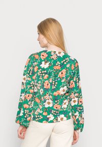 Blusa floral com fundo verde, flores laranja e brancas, mangas longas e decote arredondado.