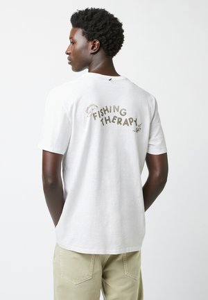 Witte katoenen t-shirt met de tekst "FISHING THERAPY" in het groen op de achterkant. Korte mouwen, relaxte pasvorm, zachte textuur, casual stijl.