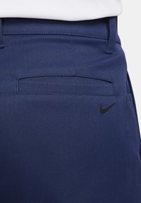 Tamsiai mėlynos kelnės su lygiu paviršiumi, su užpakaline kišenėle ir mažuoju juodu Nike logotipu dešinėje pusėje.