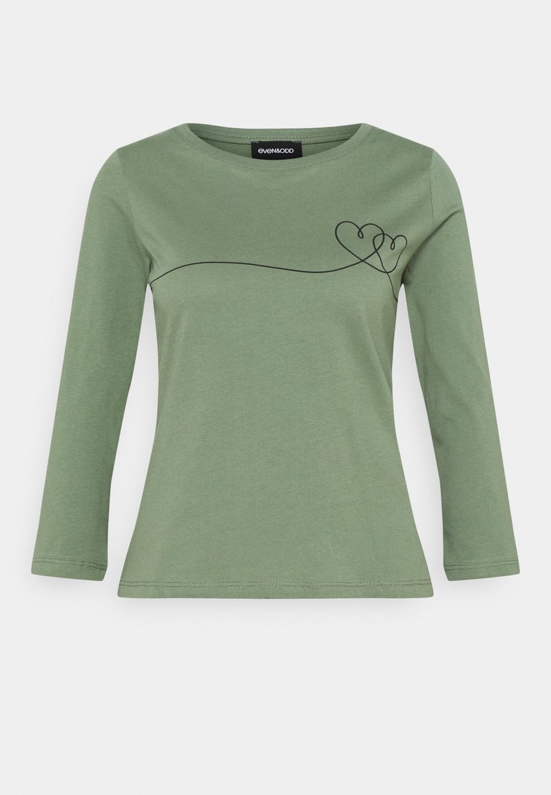 Vihreä pitkähihaisessa paidassa on pyöreä pääntie, ja etuosassa vasemmassa ylärintakehässä on mustasta, jatkuvasta viivasta muodostettu kaksi toisiinsa kytkettyä sydäntä.