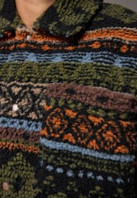 Gebreide fleece shirt met een kraagnek. Beschikt over een intricaat patroon van groene, oranje, blauwe, zwarte en bruine texturen en strepen.