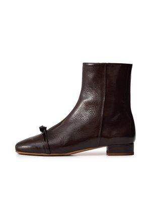 Donkerbruine leren enkellaars met een kleine blokhak en een decoratieve riem met een knoopdetail vlak bij de teen.
