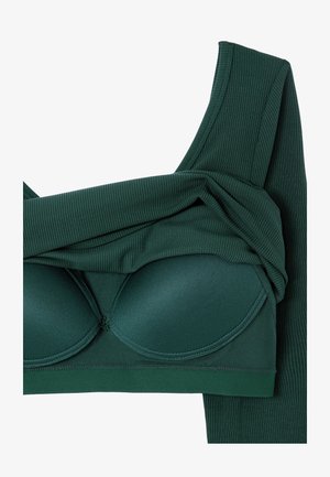 Haut en tissu côtelé vert foncé avec des bonnets amovibles et des bretelles larges, plié pour montrer la structure intérieure et la texture.