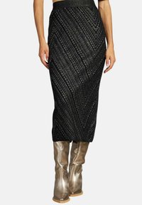 Jupe en tricot noire avec un motif en zigzag, featuring des fils métalliques. Associée à des bottes dorées brillantes jusqu'au genou. Silhouette évasée.