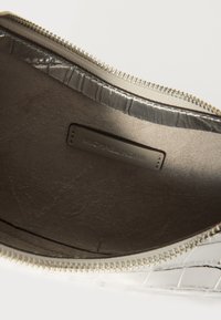 Bílá patentní kožená kabelka s texturovaným krokodýlím vzorem, se stříbrným zipem a diskrétní vnitřní etiketou s nápisem "Michael Kors."