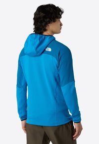 Giacca blu con cappuccio, dotata di un motivo testurizzato, maniche lunghe e logo sulla spalla. Presenta una vestibilità comoda e sezioni di tessuto a contrasto.