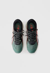 Scarpe sportive verdi e nere con tomaia in mesh, spesse stringhe nere e dettagli riflettenti. La suola presenta un motivo di grip testurizzato.