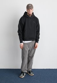 Sort hættetrøje med forlommer, grå kordfløjl bukser og sorte sneakers med hvide og beige accenter. Brun kasket med logo.