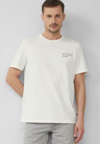 Witte katoenen t-shirt met korte mouwen, ronde hals en zwarte tekst op de linkerkant van de borst, met een humoristisch bericht over ingrediënten.