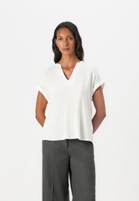 Weißes T-Shirt mit kurzen Ärmeln und V-Ausschnitt, aus leichtem Material gefertigt. Glatte Textur, lockere Passform, kombiniert mit grauen Nadelstreifenhosen.