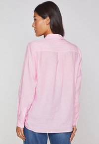 Chemise rose clair à manches longues avec des rayures verticales blanches, poignets boutonnés et un détail de empiècement au dos, fabriquée dans un tissu doux et respirant.