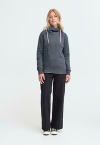 Grijze sweatshirt met een kraag, trekkoorden en leren accenten, gecombineerd met zwarte wijde broek en sneakers. Eenvoudig, casual ontwerp.