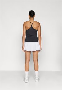 Fekete sportos ujjatlan trikó vékony pántokkal, fehér redőzött szoknyával párosítva. Fehér edzőcipők és zoknik teszik teljessé a sportos megjelenést.