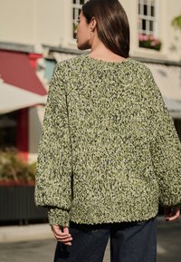 Strikket, oversized sweater i grøn med sorte prikker. Har sænkede skuldre og ribbet kant, der giver en behagelig pasform.