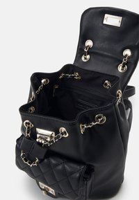 Sac à dos en cuir noir avec cordon de serrage, ferrures dorées, détails en chaîne et une poche matelassée. Le haut ouvert révèle un intérieur spacieux.