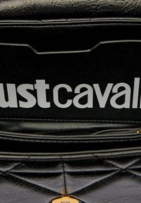 Borsa sintetica nera trapuntata con finitura testurizzata e accessori dorati. Presenta un logo bianco prominente "Just Cavalli" sulla patta.