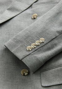 Manche de blazer en tissu gris texturé avec cinq boutons beige clair et de fins détails de couture. Comprend une petite poche sur la manche.