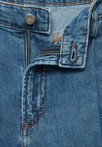 Jean en denim avec un délavage bleu, doté d'une fermeture à bouton métallique, d'une braguette zippée et de coutures et poches contrastées en orange.
