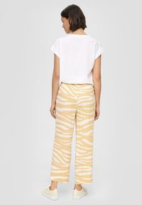 Witte kortslippige shirt, gele broek met witte zebra-strepen, losse pasvorm, enkellengte, gecombineerd met lichte sneakers.
