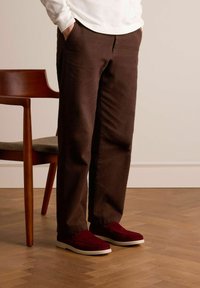 Brown textured pants with a loose fit, paired with burgundy slip-on shoes featuring a white sole. A wooden chair is in the background.