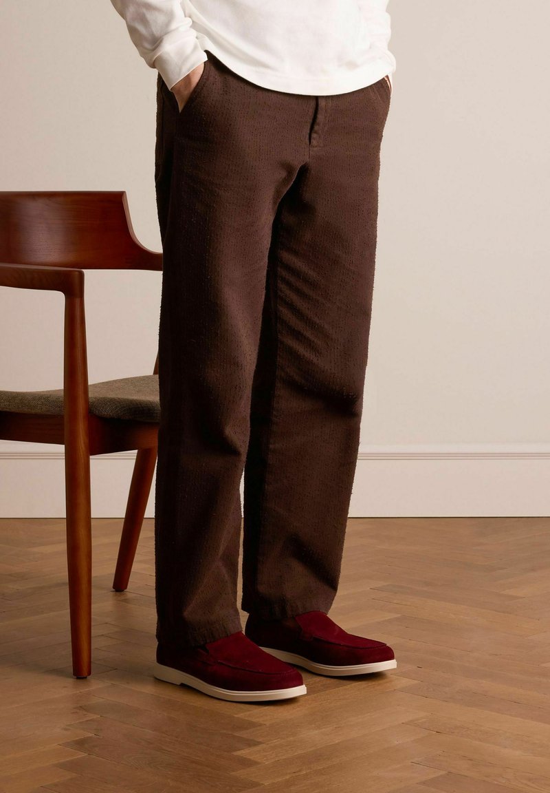 Brown textured pants with a loose fit, paired with burgundy slip-on shoes featuring a white sole. A wooden chair is in the background.