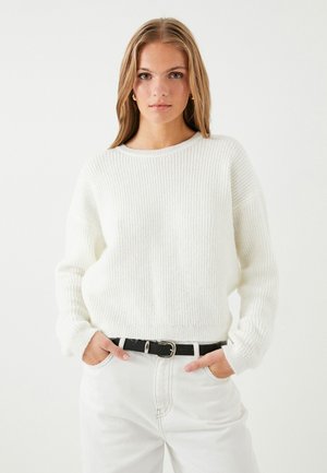 Weißer gerippter Pullover mit Rundhalsausschnitt, lockerer Passform und langen Ärmeln, kombiniert mit hochgeschnittenen weißen Jeans und einem schwarzen Gürtel.