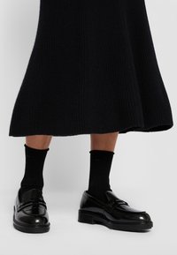 Loafers negri din piele lăcuită, cu un finisaj strălucitor, având o curea decorativă. Purtați cu șosete negre până la gleznă, asortate cu o fustă neagră cu nervuri.