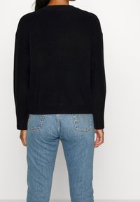 Schwarzer, übergroßer Pullover aus weichem Strick mit überschnittenen Schultern. Getragen mit hellblauen, hoch taillierten Jeans, die ein klassisches Taschendesign aufweisen.