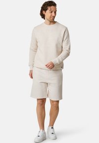 Ljust beige sweatshirt och matchande shorts i mjukt tyg. Har rundad halsringning, framficka och subtila sömmar.