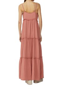 Maxikleid aus weichem, strukturiertem Roststoff. Verfügt über dünne Träger, gestufte Rüschen und eine fließende Silhouette, die bis zur Mitte der Wade reicht.