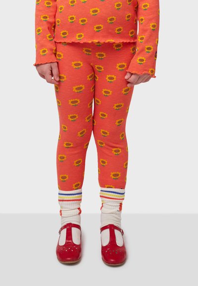 Bright orange ribbed leggings and matching long-sleeve top with yellow sunflower pattern. Red shoes with white accents; striped socks.