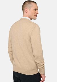 Pull beige en maille avec un col rond, des poignets et un ourlet côtelés, présentant une texture douce et une silhouette ajustée.