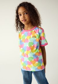 Maglietta a maniche corte in morbido cotone, con una palette di colori pastello, motivi a cuore e un piccolo ricamo di un arcobaleno vicino allo scollo.