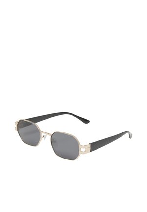 Lunettes de soleil avec verres sombres octogonaux, montures en métal doré et branches en plastique noir inclinées vers l'extérieur sur fond blanc.