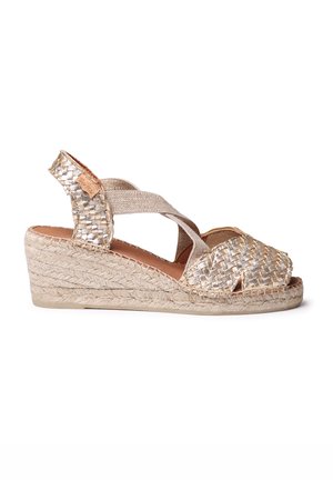 Sandal med kilehæL, der har et vævet gyldent overdel og beige stofstropper. Den har en flettet jute sål og åben tå-design.