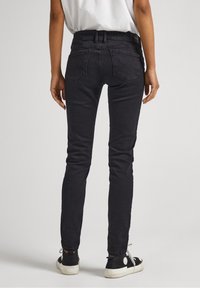 Jeans negros ajustados con una cintura alta, dos bolsillos traseros y un acabado texturizado sutil. Llevados con zapatillas casuales.